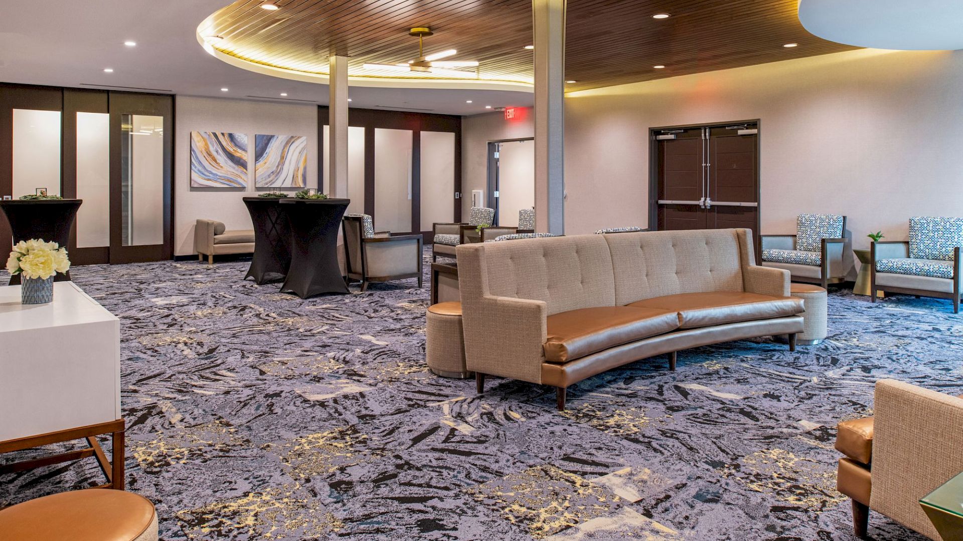 The image shows a modern, well-lit lobby with comfortable furniture, stylish decorations, and a wooden ceiling accent.