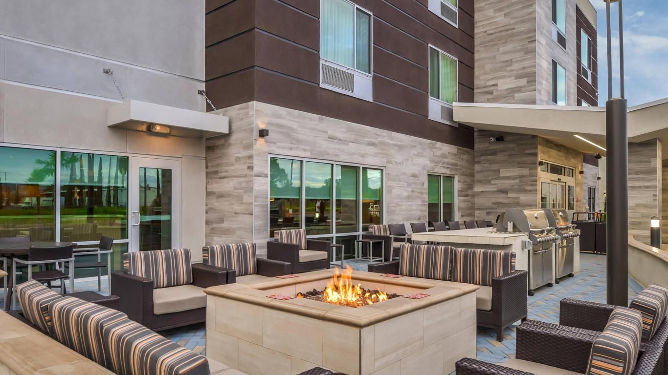 Outdoor patio with modern seating, a central fire pit, a grill area, and contemporary building facade in the background, ideal for social gatherings.