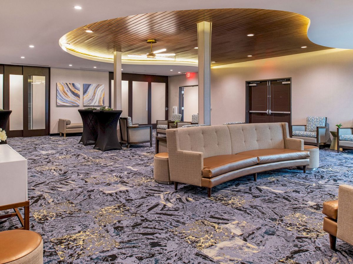 This image shows a lobby area with modern furnishings, including sofas, chairs, and tables, complemented by abstract art and a patterned carpet.