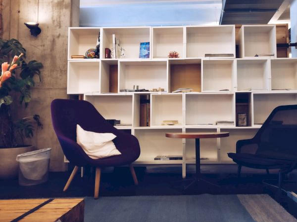 A cozy room with a bookshelf, purple and black chairs, a small table, potted plants, and soft lighting ends the sentence.