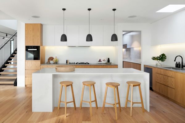 A modern kitchen with wooden floors, an island with stools, white cabinets, a black sink, and pendant lights over the island.