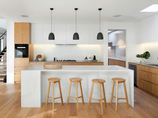 A modern kitchen with wooden floors, an island with stools, white cabinets, a black sink, and pendant lights over the island.
