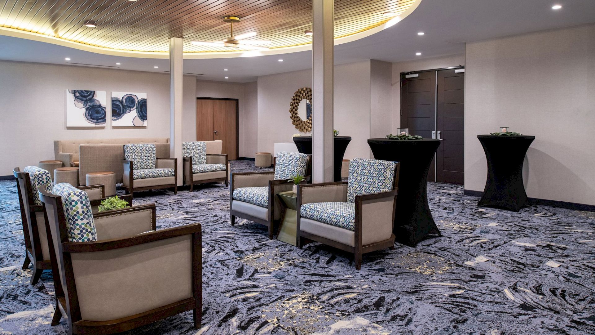 A modern, well-lit lounge area with stylish chairs, round tables, and elegant decor featuring abstract art and a mirror on the wall.