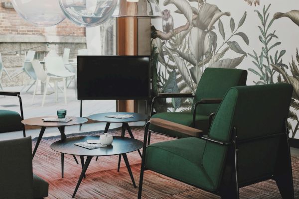 A modern living room with green chairs, a TV, a coffee table, and a botanical wallpaper, illuminated by large pendant lights.