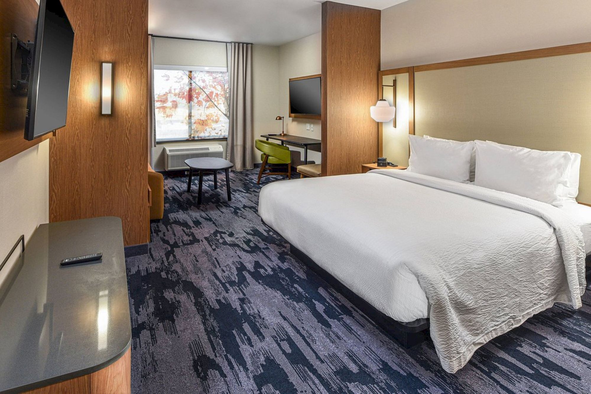 This image shows a modern hotel room with a large bed, flat-screen TV, desk, chair, and window with curtains. The room features contemporary decor.