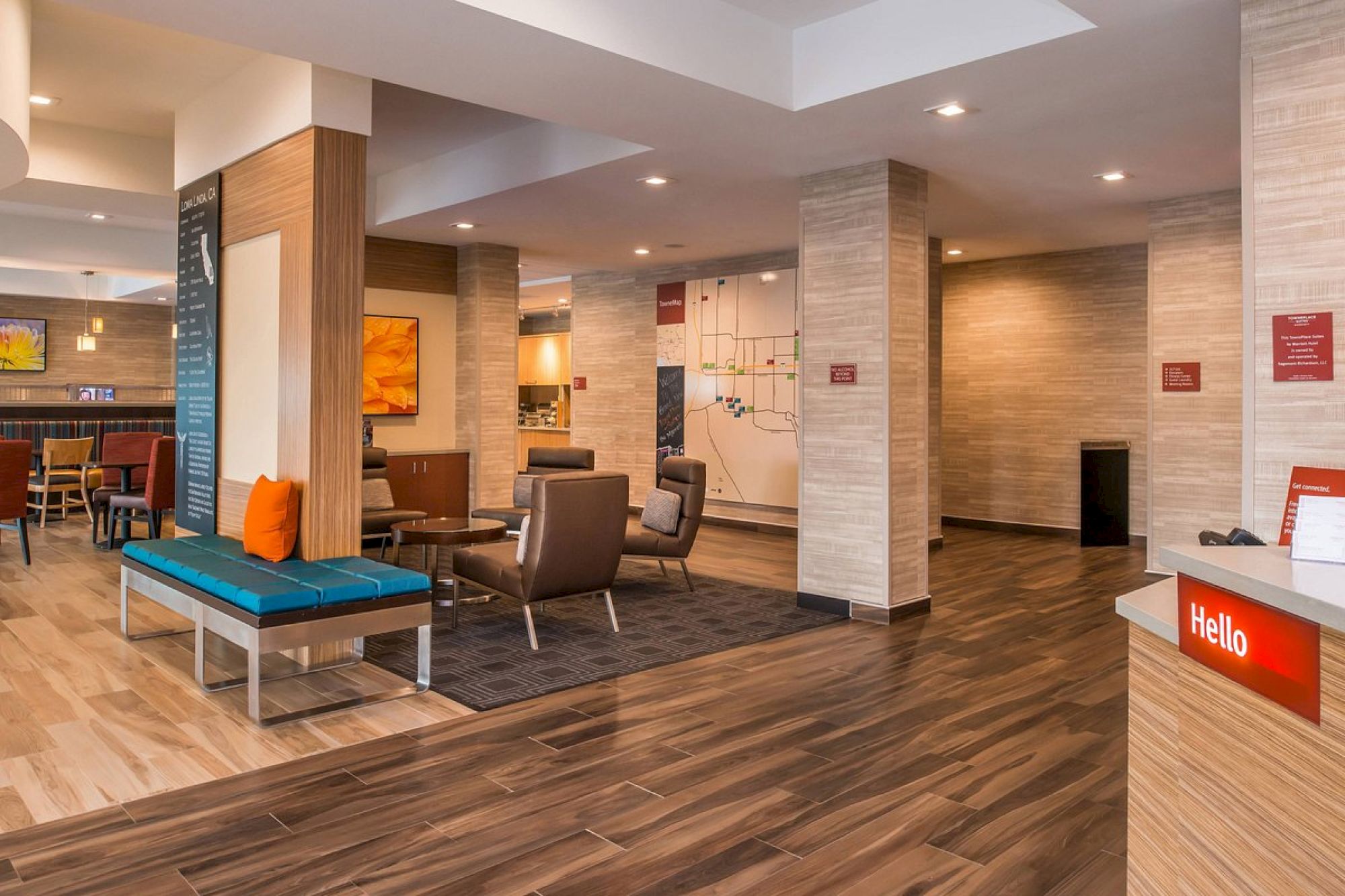 A modern lobby area with seating, artwork, a check-in desk, and wooden flooring is shown. The space has contemporary decor with warm lighting.