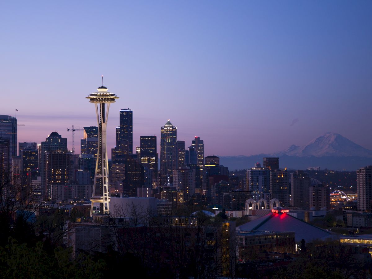 The image shows the Seattle skyline at dusk with the Space Needle prominently featured and Mount Rainier in the background.