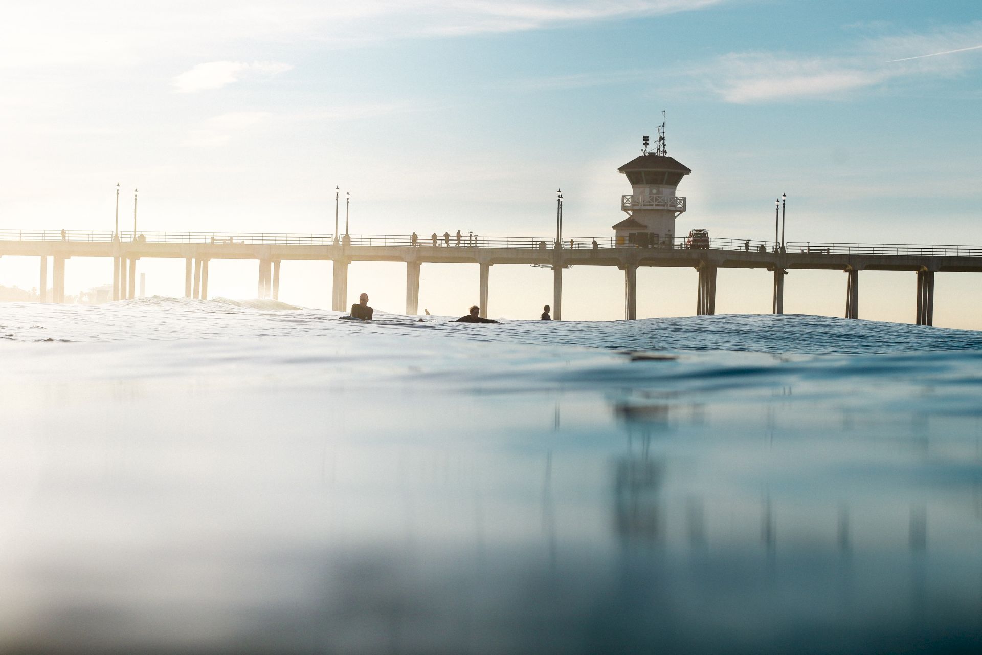 This image shows a serene ocean view with a long pier extending into the water and people walking on it, under a clear blue sky.